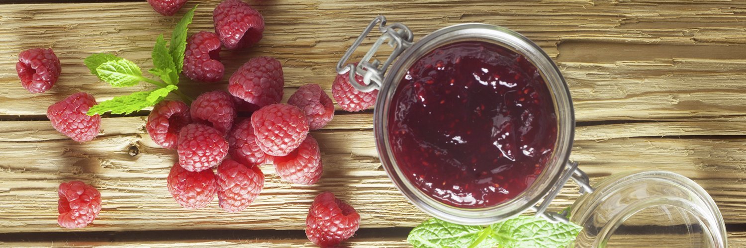 Fruchtaufstrich und Himbeeren liegen auf einem Holzbrett.