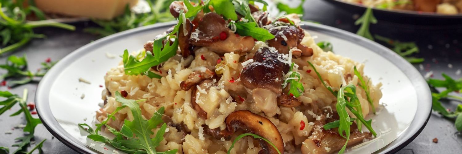 Auf einem Teller ist ein Pilzrisotto mit Parmesan und Rucola als Topping angerichtet.