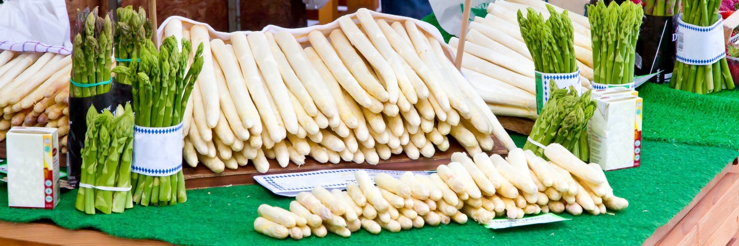 Grüner und weißer Spargel liegen in der Auslage eines Marktstandes.