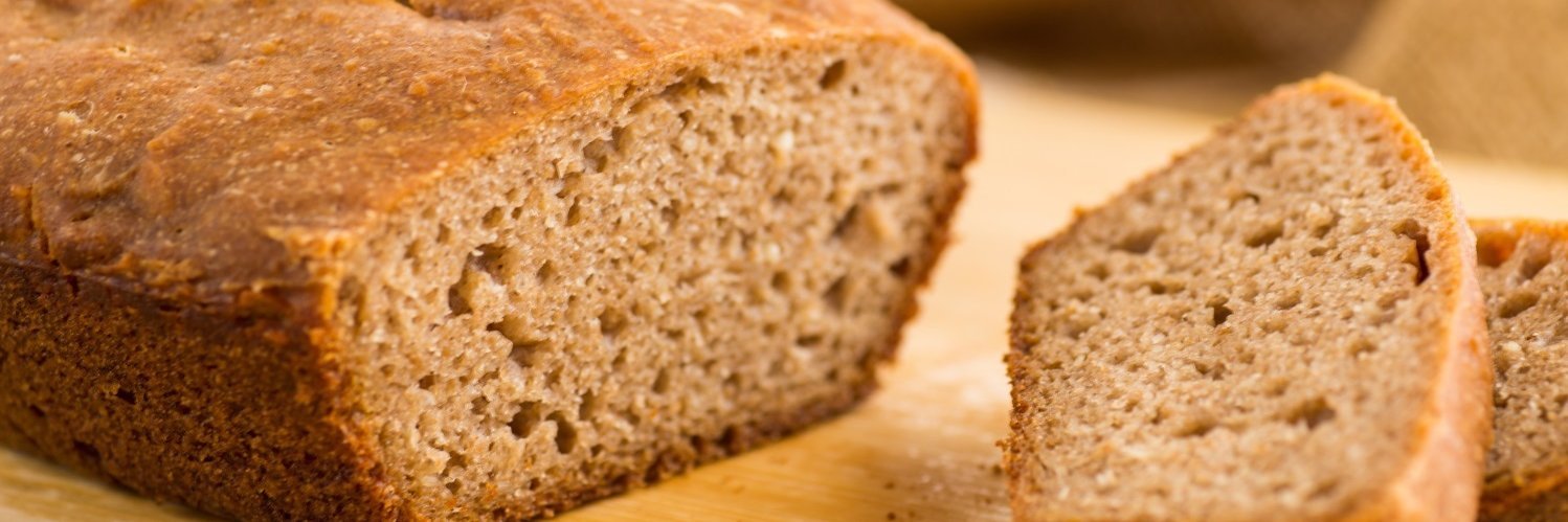 Auf einem hellen Holzbrett liegt ein aufgeschnittenes Vollkornbrot.