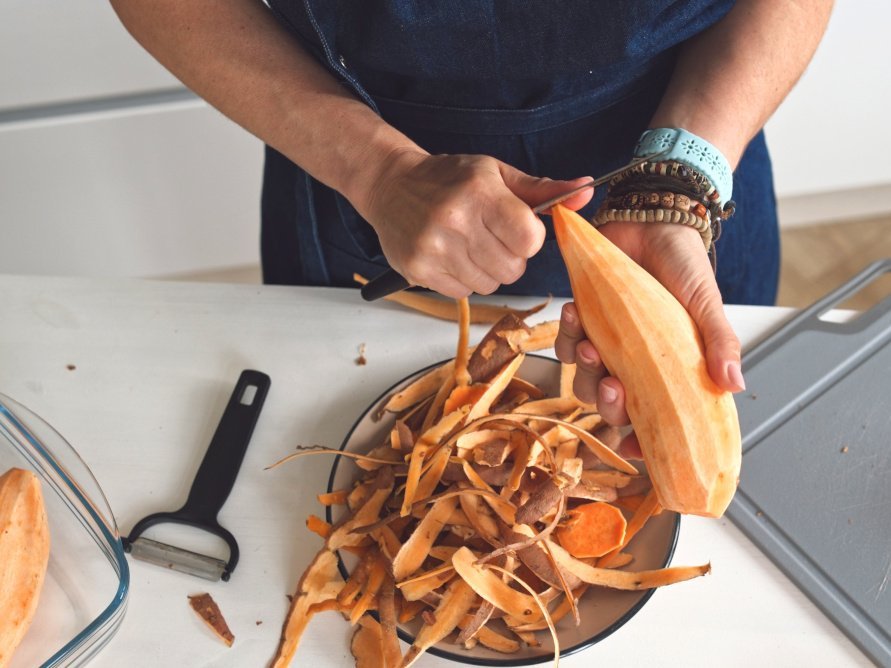 Person schält eine große Süßkartoffel.