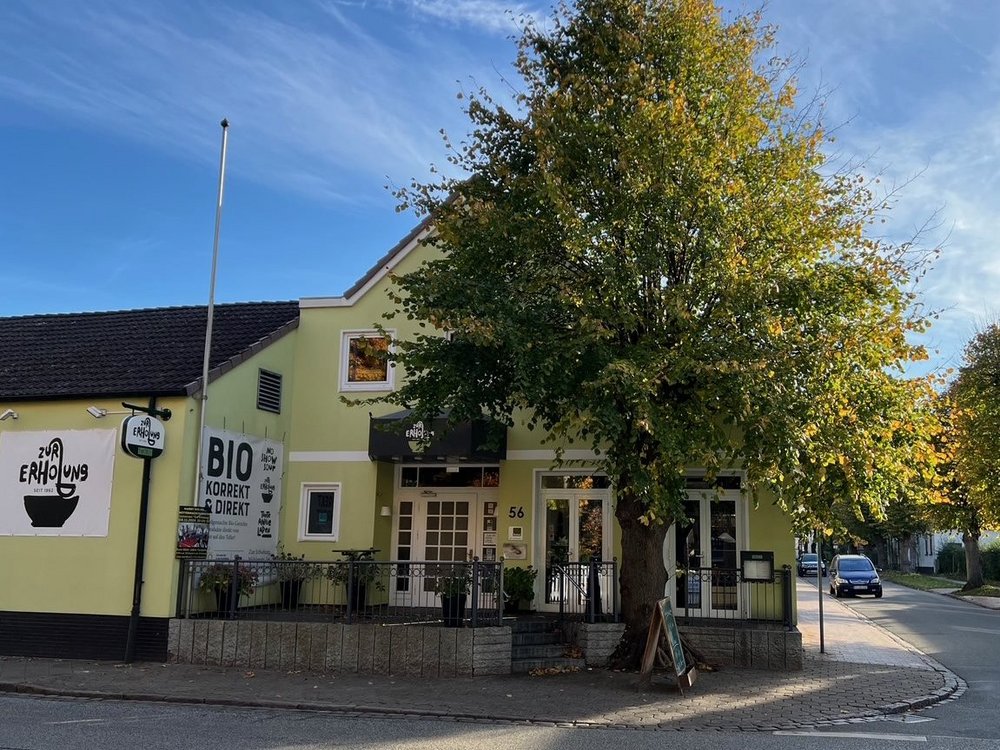Vor einer gelben Gastwirtschaft steht ein Lindenbaum.