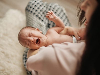 Baby liegt in Mamas Arm und schreit.