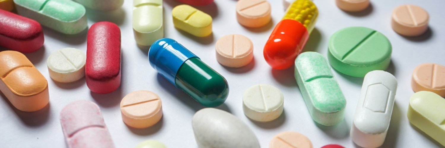Eine helle Fläche ist bedeckt mit unterschiedlichen Tabletten und Kapseln in bunten Farben.