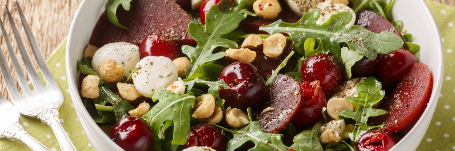 Auf einem Tisch steht eine weiße Schüssel mit Rucola, Roter Bete, Mozzarella und Haselnüssen.