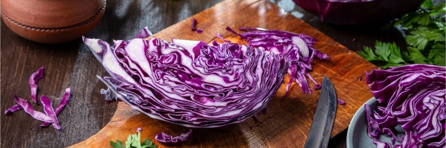 Auf einem Tisch liegt ein aufgeschnittener Rotkohl, ein Viertel davon liegt auf einem Holzbrett.