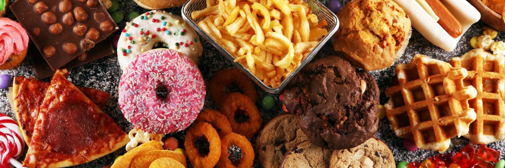 Pizzastücke, Donuts, Pommes Frites und ander Süßigkeiten sind auf einem Tisch verteilt.