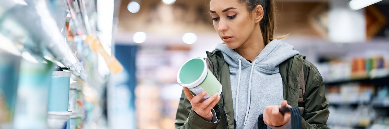 Eine junge Frau liest beim Kauf eines Milchprodukts im Supermarkt das Produktetikett.