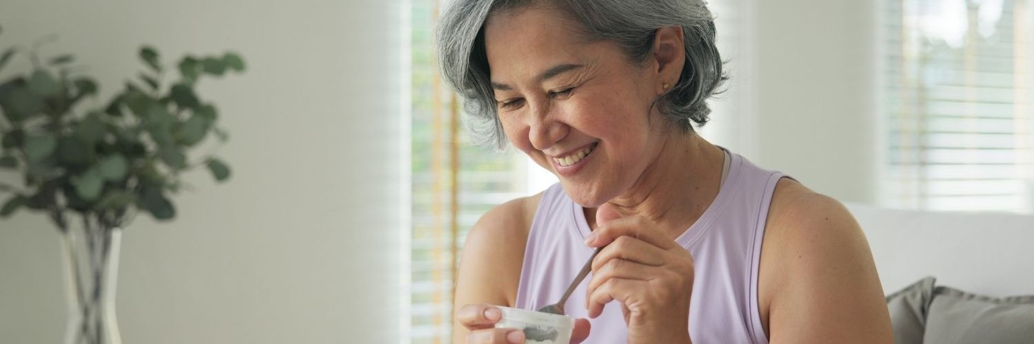 Eine etwa 50-jährige Frau isst einen Joghurt. 