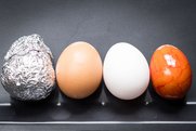 Vier Eier liegen nebeneinander auf einem Blech: eins aus Alu, ein braunes, ein weißes und ein orange gefärbtes Osterei.