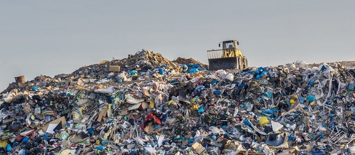 Bagger steht auf einem Müllberg mit viel Plastik