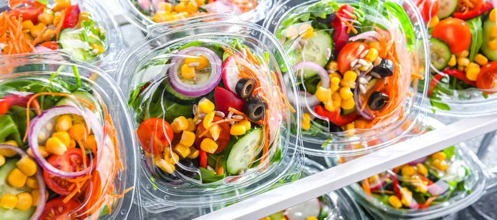 Verzehrfertige Salatmischungen in Plastikschalen liegen im Kuehlregal.