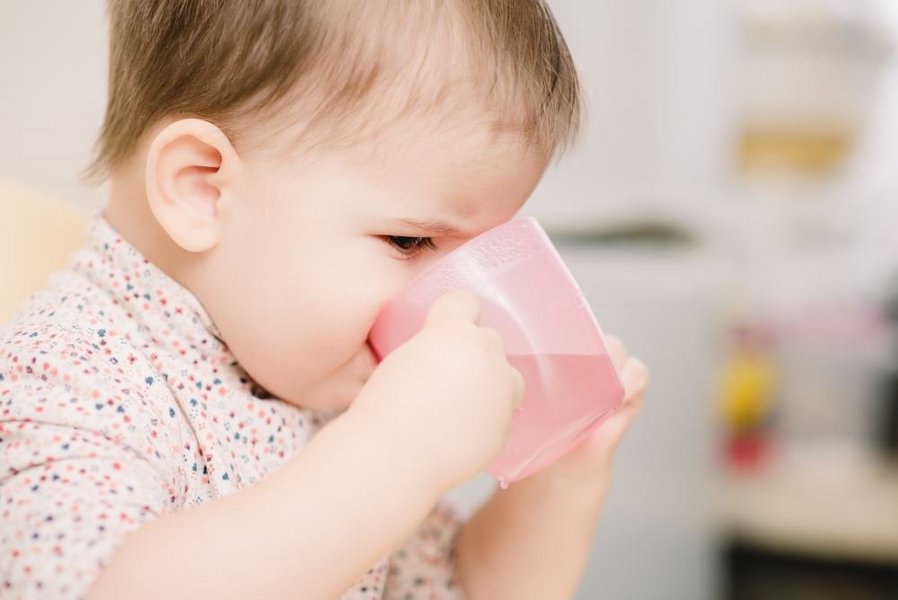 Ein Baby trinkt Wasser aus einem Becher.