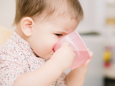 Ein Baby trinkt Wasser aus einem Becher.