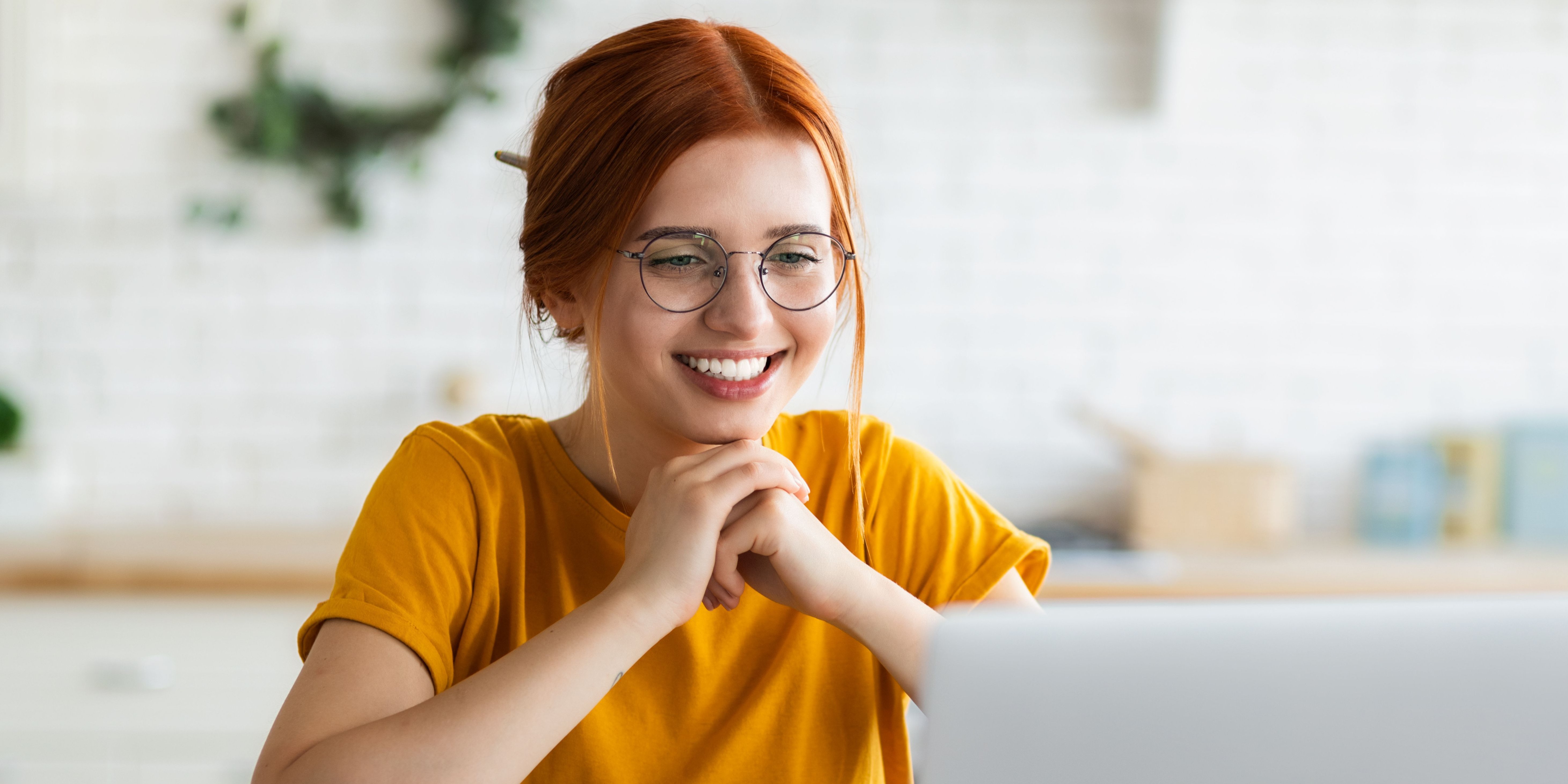 Junge Frau mit Tasse und Buch vor sich schaut auf Laptop.. Artikel "Web-Seminare" öffnen.