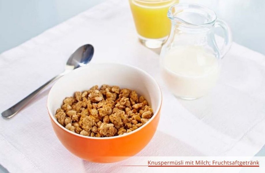 Schale mit Knuspermüsli, Löffel, Glas Saft und Krug mit Milch.