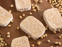 Abgebildet sind mehrere Scheiben Tempeh und einzelne Sojabohnen.