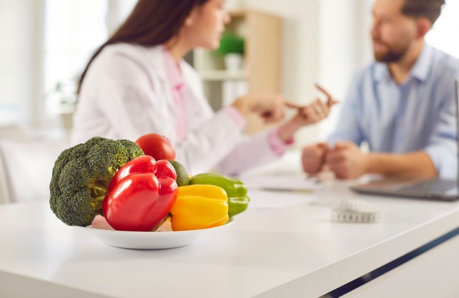 Eine Ernährungsberaterin berät einen jungen Mann. Im Vordergrund ist eine Teller gefüllt mit frischem Gemüse.