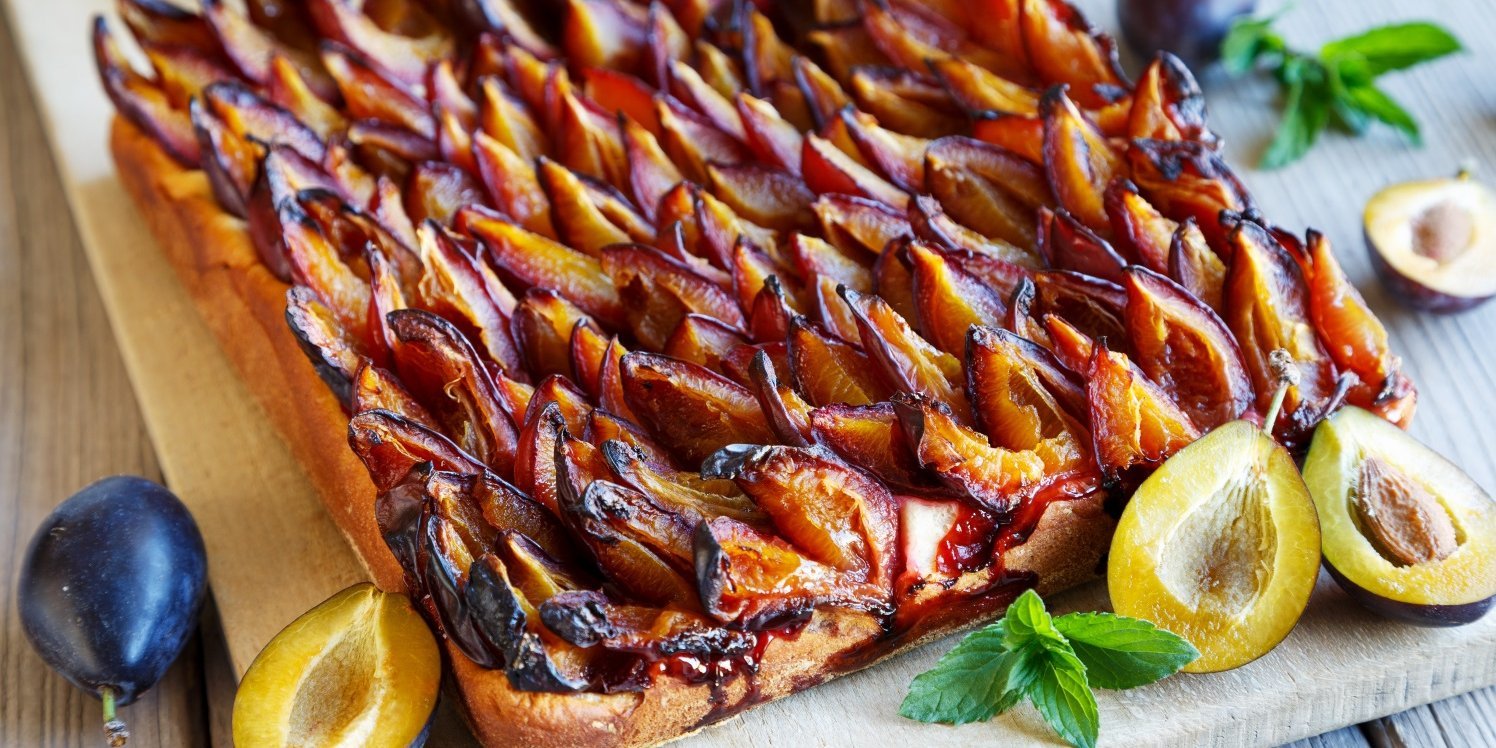 Auf einem Holzbrett liegt ein Blechkuchen mit Zwetschen, daneben liegen ganze und halbierte Früchte.. Artikel "Zwetschge auch herzhaft genießen" öffnen.
