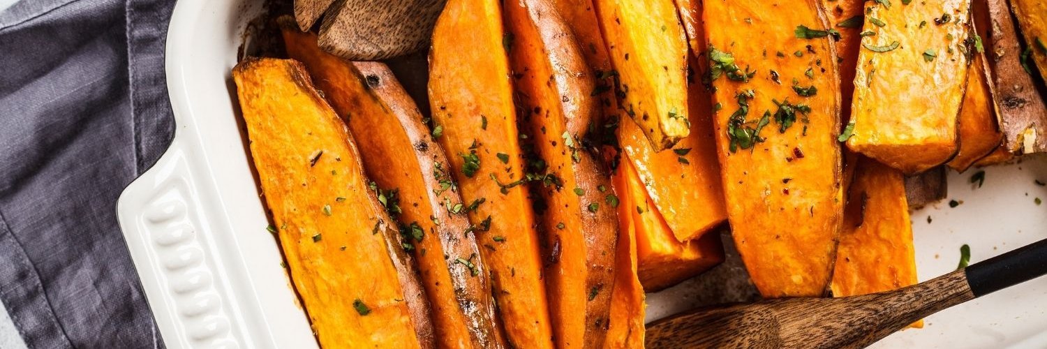 In einer Ofenform liegen geviertelte gebackene Süßkartoffeln mit Kräutern bestreut.