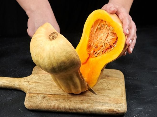 Ein Butternut-Kürbis wird mit einem Messer halbiert. Das Kürbisinnere ist orange.