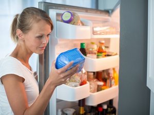 Eine Frau steht am geöffneten Kühlschrank und kontrolliert die Haltbarkeit eines verpackten Lebensmittels.