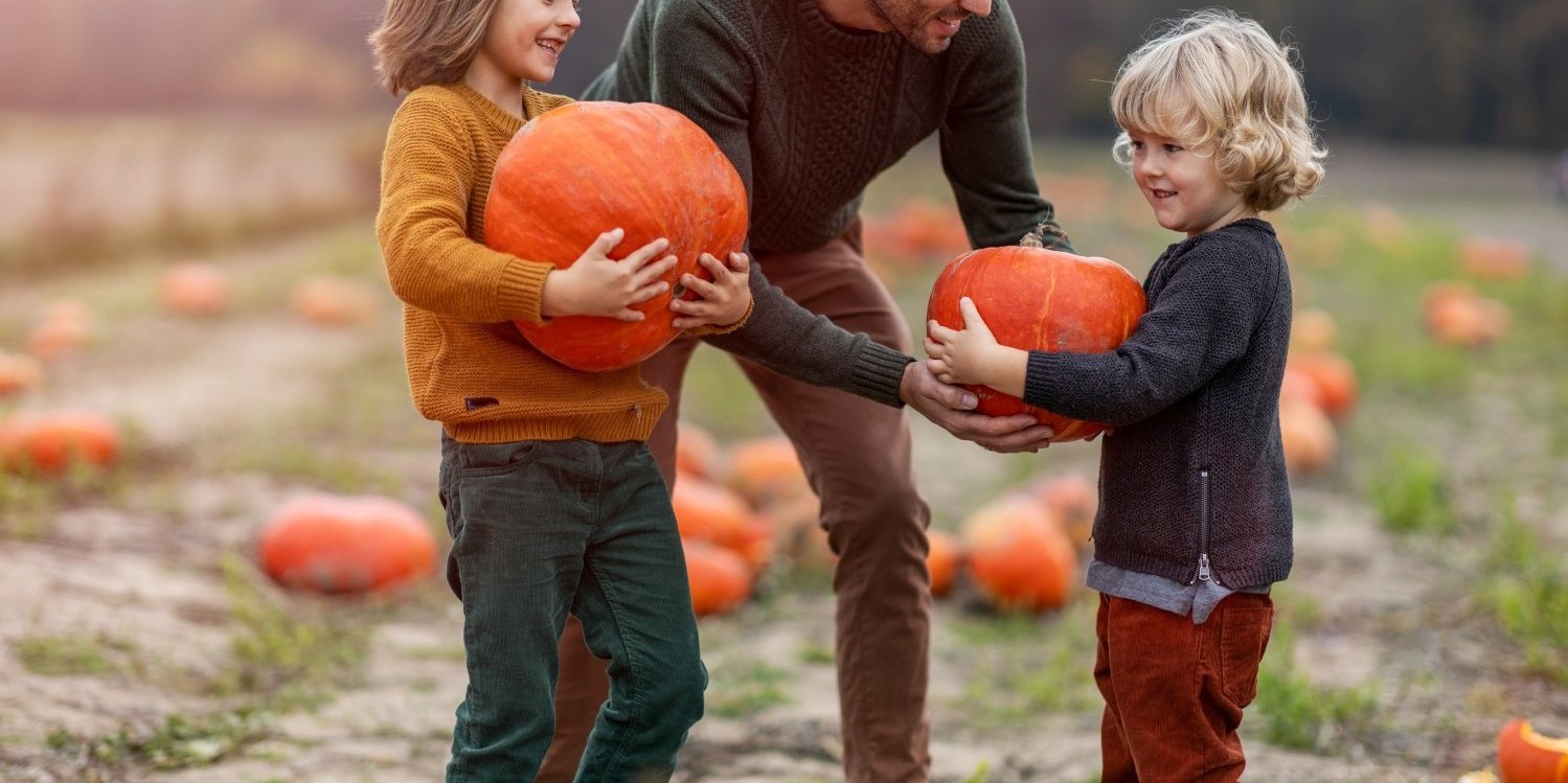 Ein Vater ist mit seinen zwei Kindern auf einem Kürbisfeld. Beide Kinder halten je einen großen Kürbis.. Artikel "Kürbisse: Gesundheit und Umwelt" öffnen.