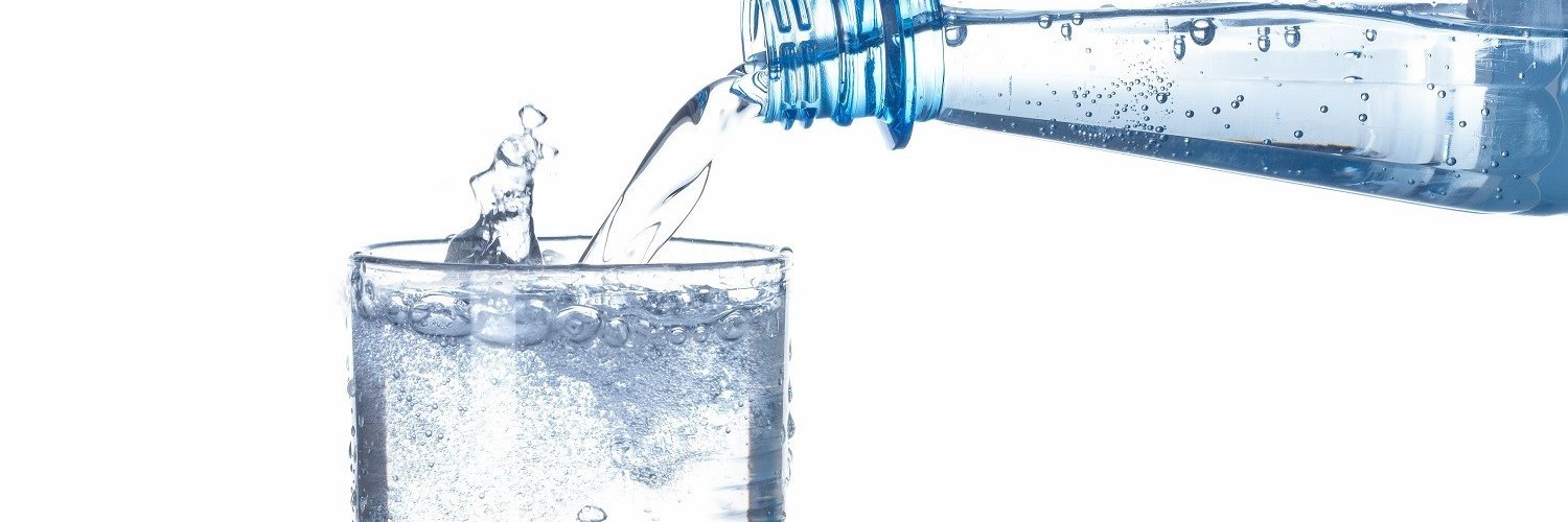 Aus einer Flasche wird Mineralwasser mit Kohlendioxid in ein Glas gegossen.