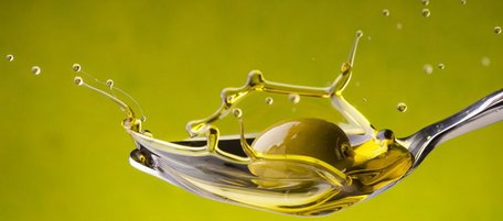 Olive fällt auf Löffel mit Olivenöl, es spritzt in alle Richtungen