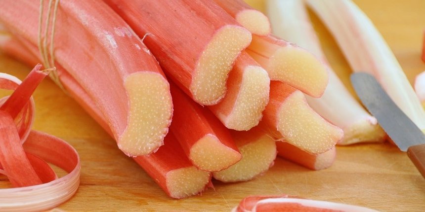 Auf einem Holztisch liegen angeschnittene Rhabarberstangen. Davor liegen Rhabarberschalen und daneben ein Messer.  . Artikel "Frühlingsgenuss von der Stange" öffnen.