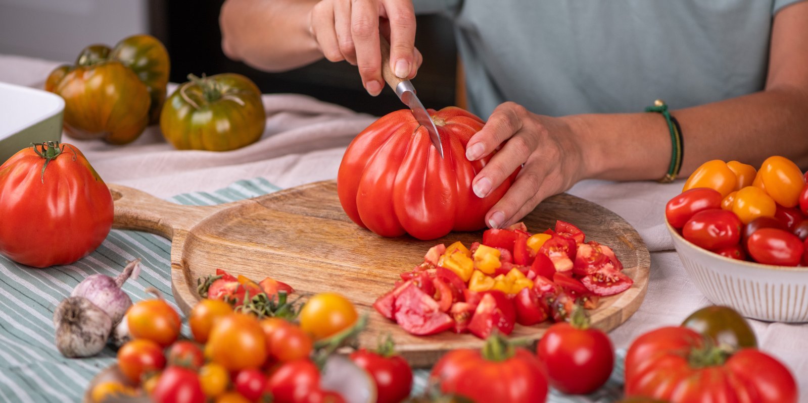 Person schneidet eine große, gerippte Tomate auf einem Holzbrett.. Artikel "Tomaten: Vom Einkauf in die Küche" öffnen.