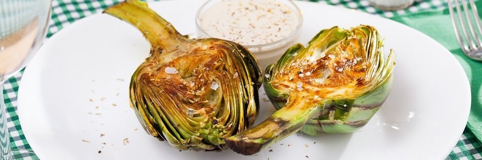 Zwei halbe gegrillte Artischocken auf einem Teller.