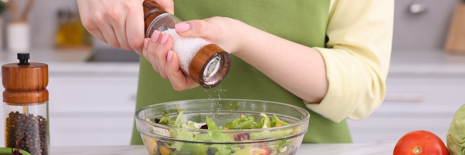 Eine Frau gibt mit einer Salzmühle Salz an eine Schüssel mit Salat. 