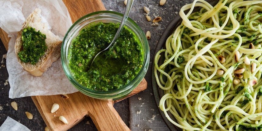 In einem Glasgefäß ist selbstgemachtes Bärlauch-Pesto. Rechts daneben steht ein Teller mit Spaghetti angerichtet mit dem Pesto. Und links daneben liegt eine Scheibe Baguette bestrichen mit dem Pesto. . Artikel "Zeit für Bärlauch-Pesto" öffnen.