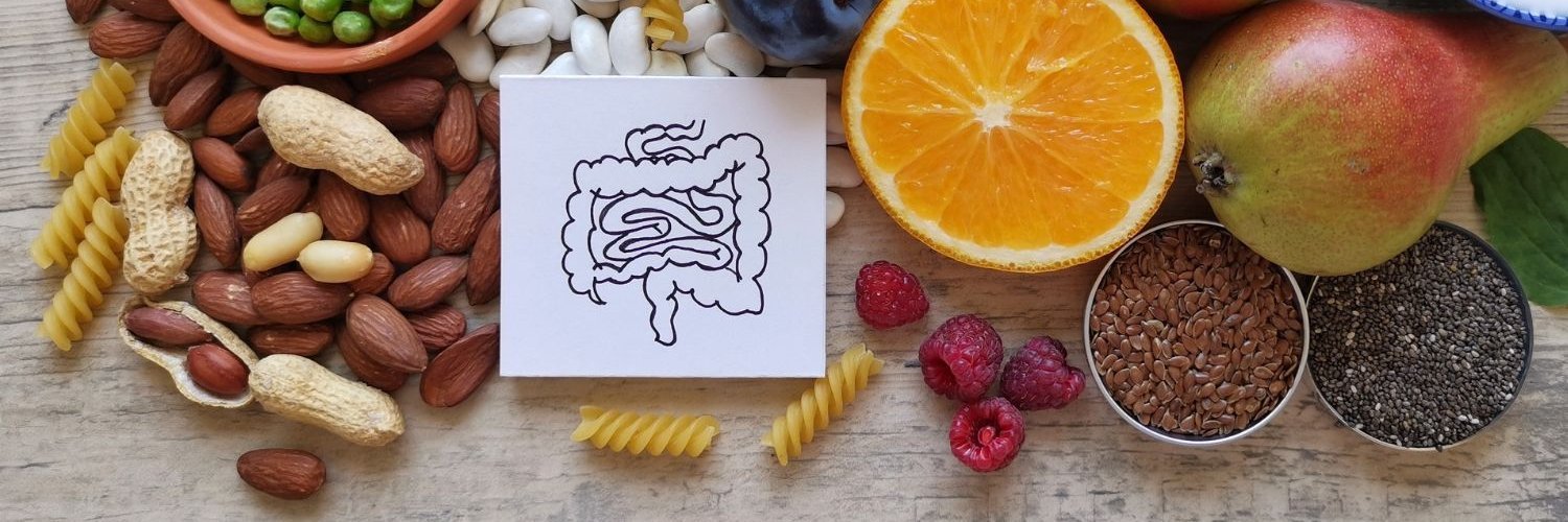 Auf einem Tisch liegen Obst, Hülsenfrüchte, Nüsse und Samen und eine Skizze des menschlichen Darms in der Mitte.