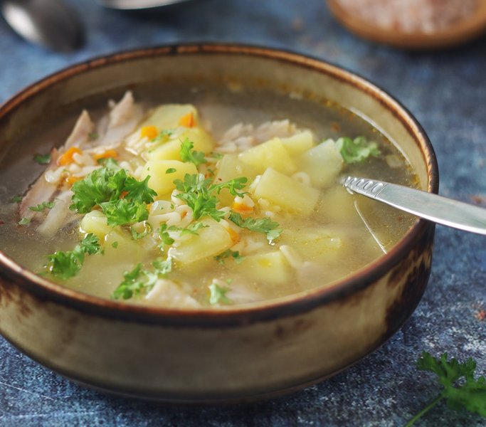 Eine Schale mit Suppe mit Kartoffelstückchen und Hühnchen steht auf dem Tisch.