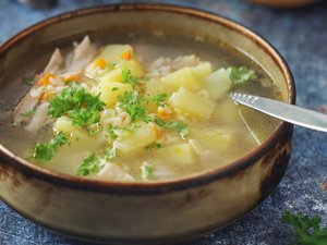 Eine Schale mit Suppe mit Kartoffelstückchen und Hühnchen steht auf dem Tisch.