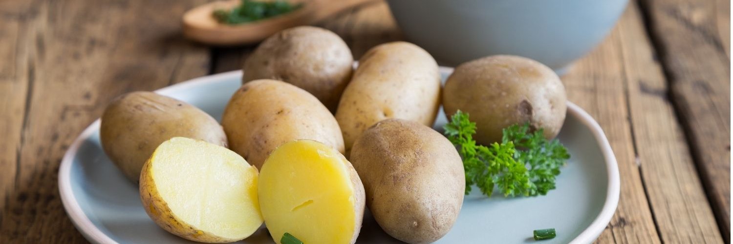 Auf einem dunklen Holztisch steht ein weißer Teller mit ganzen und halbierten Pellkartoffeln, daneben eine Schale mit Kräuterquark.