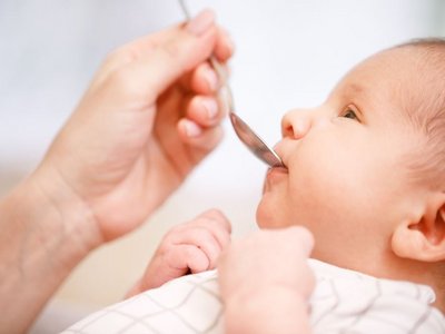 Ein Baby wird mit einem Löffel Vitamintropfen in den Mund gegeben.
