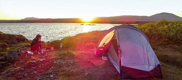 Eine Person hat ein Zelt auf einer Wiese vor einem See aufgeschlagen