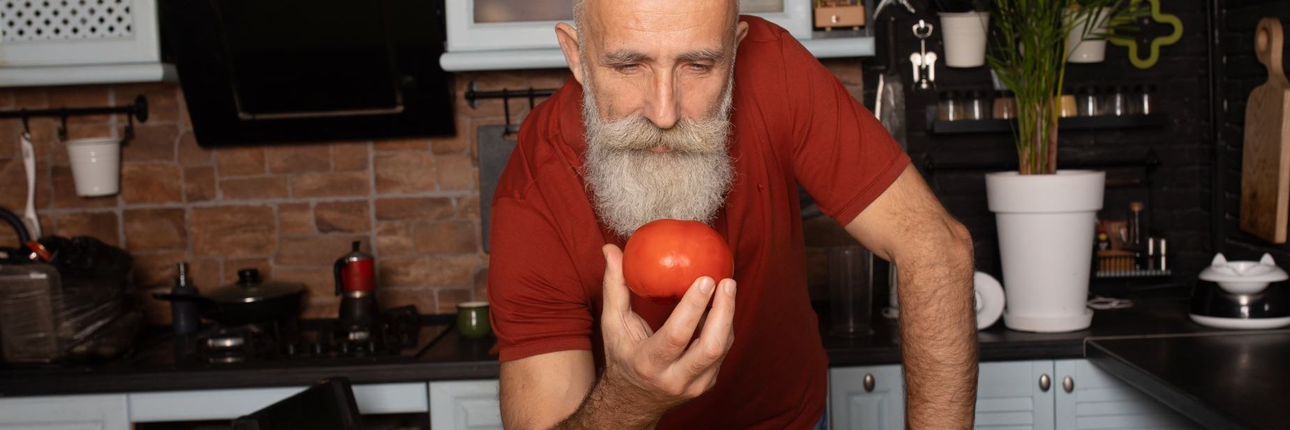 Ein Mann betrachtet eine Tomate in seiner Hand.