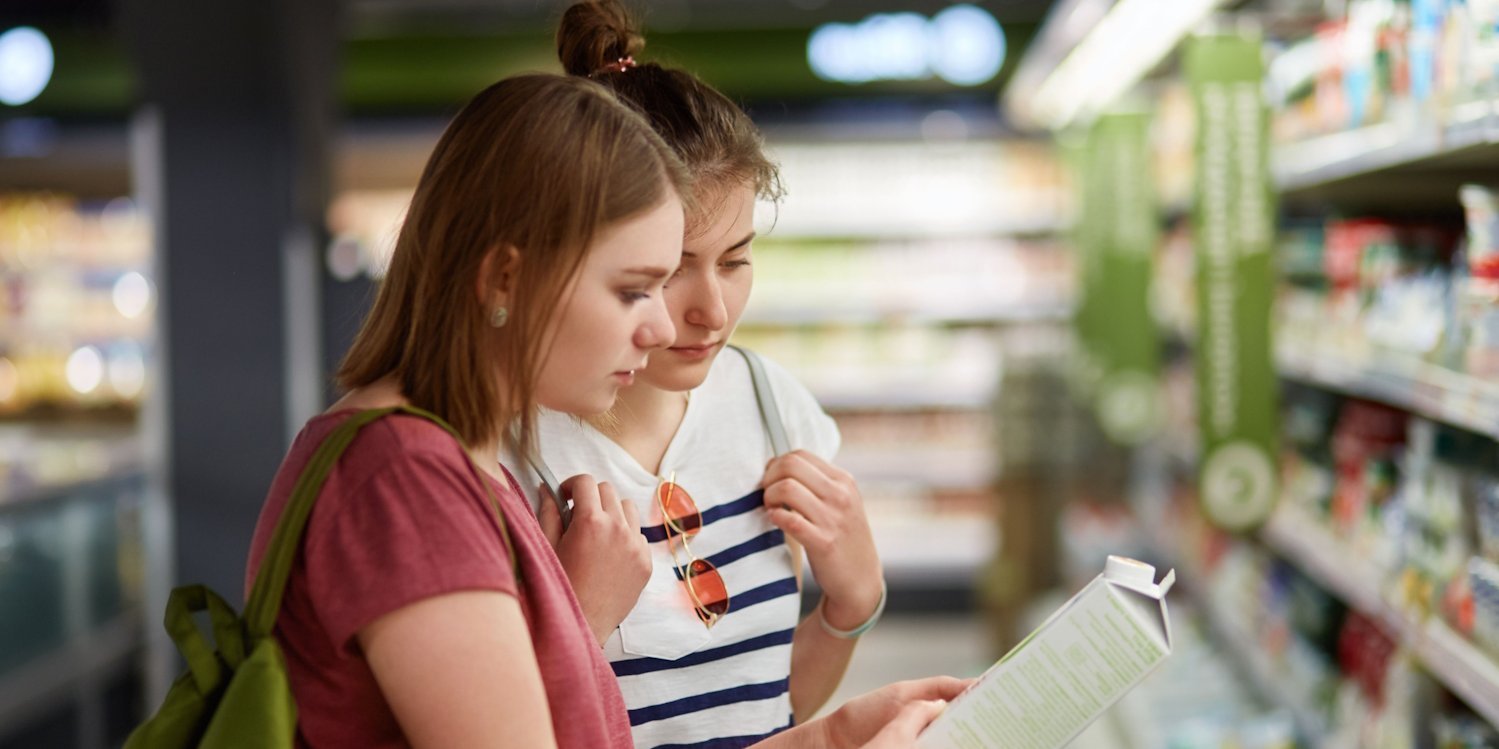 Zwei junge Frauen betrachten eine Milchpackung vor einem Kühlregal.. Artikel "Milch: Vom Einkauf in die Küche" öffnen.
