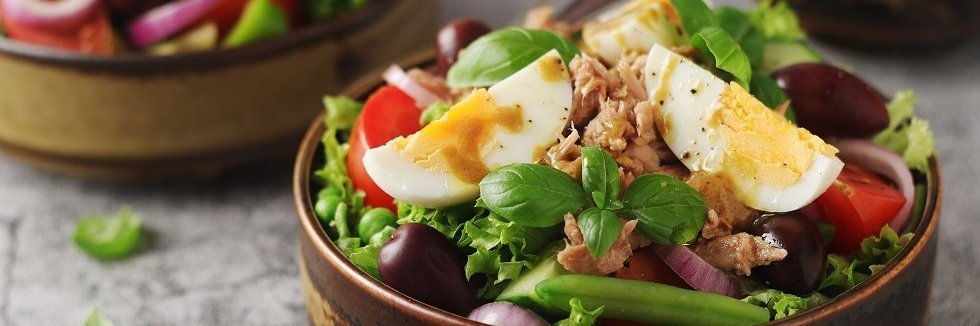 Eine Schale Salat mit grünem Salat, Tomaten, grüne Bohnen, Oliven, Zwiebeln, Thunfisch und hartgekochtem Ei. 