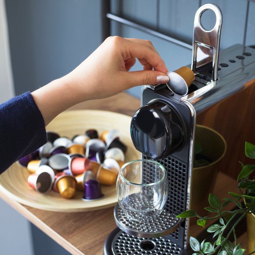 Eine Person legt eine Alu-Kaffeekapsel in einen Kaffeeautomaten ein.