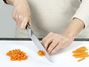 Person schneidet Möhren mit einem Messer in Wüfelstücke.