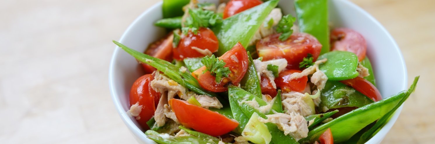 In einer weißen Schüssel ist ein Salat aus Zuckerschoten, Kirschtomaten, Thunfisch und Petersilie angerichtet.