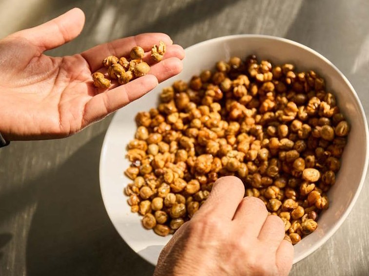 Ein Hand nimmt geröstete Ackerbohnen aus einer weißen Schüssel.