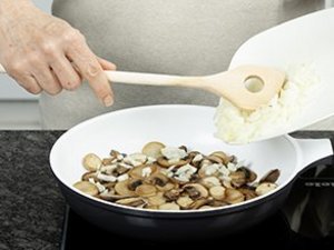 Eine Person brät Pilze und Zwiebeln in Pfanne.