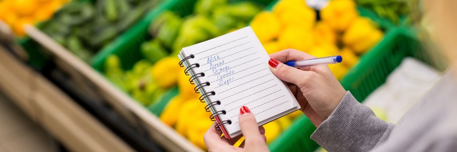Eine Nahaufnahme von Frauenhänden mit einer Einkaufsliste in einem Notizbuch im Supermarkt.