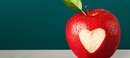 Apfel mit eingeschnittenem Herz vor einer Tafel
